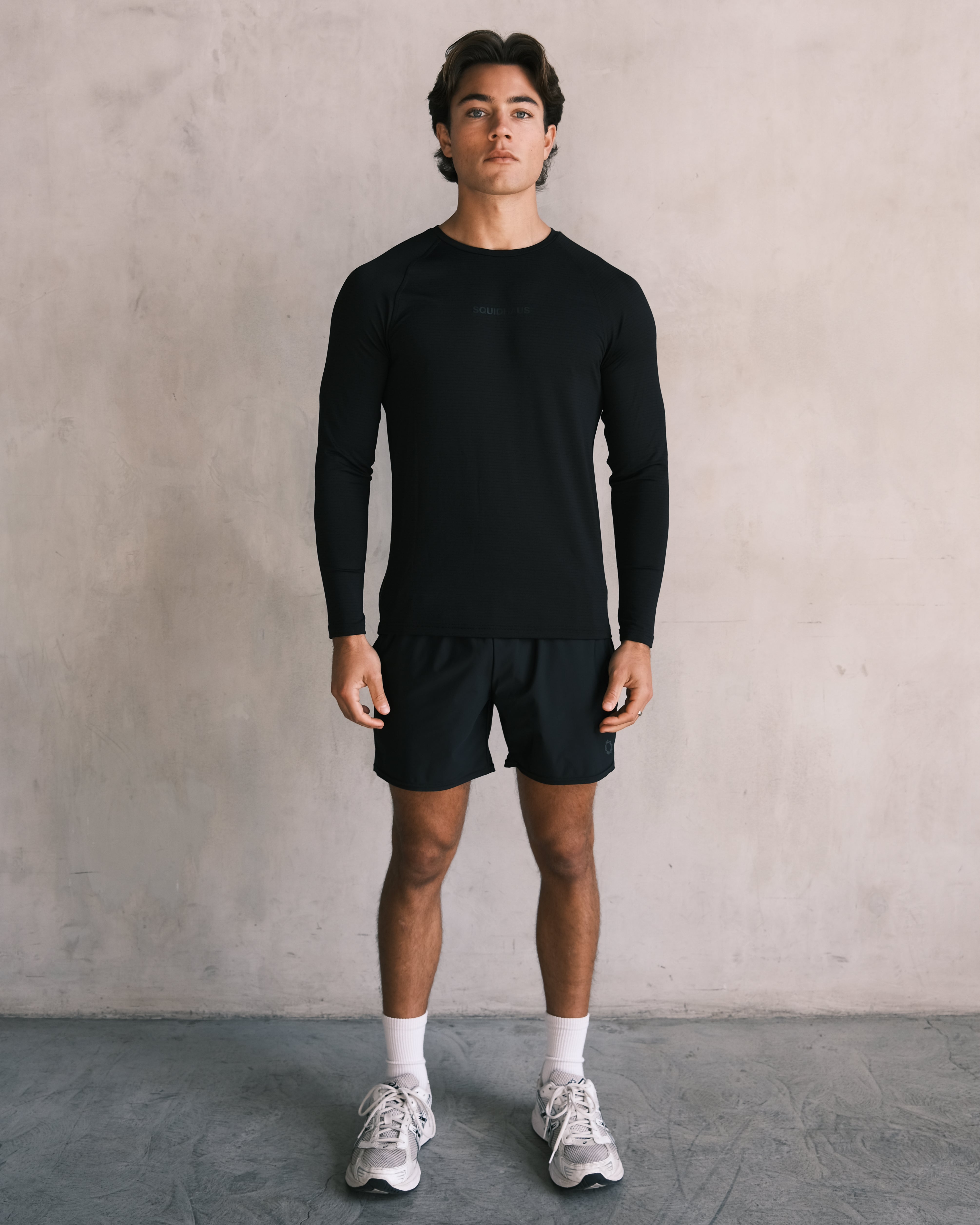 A man wearing the black Essentials Longsleeve Athletic Fitted Tee with the black 5" inseam Essentials Shorts from Squidhaus