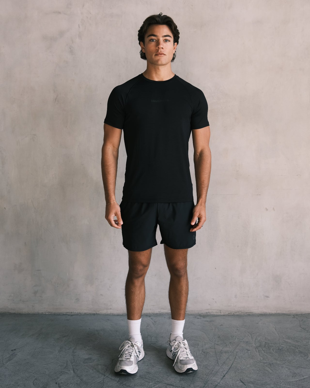 A man wearing the Squidhaus Essentials Short Sleeve Athletic Fitted Tee with 5" inseam Essential Shorts in black