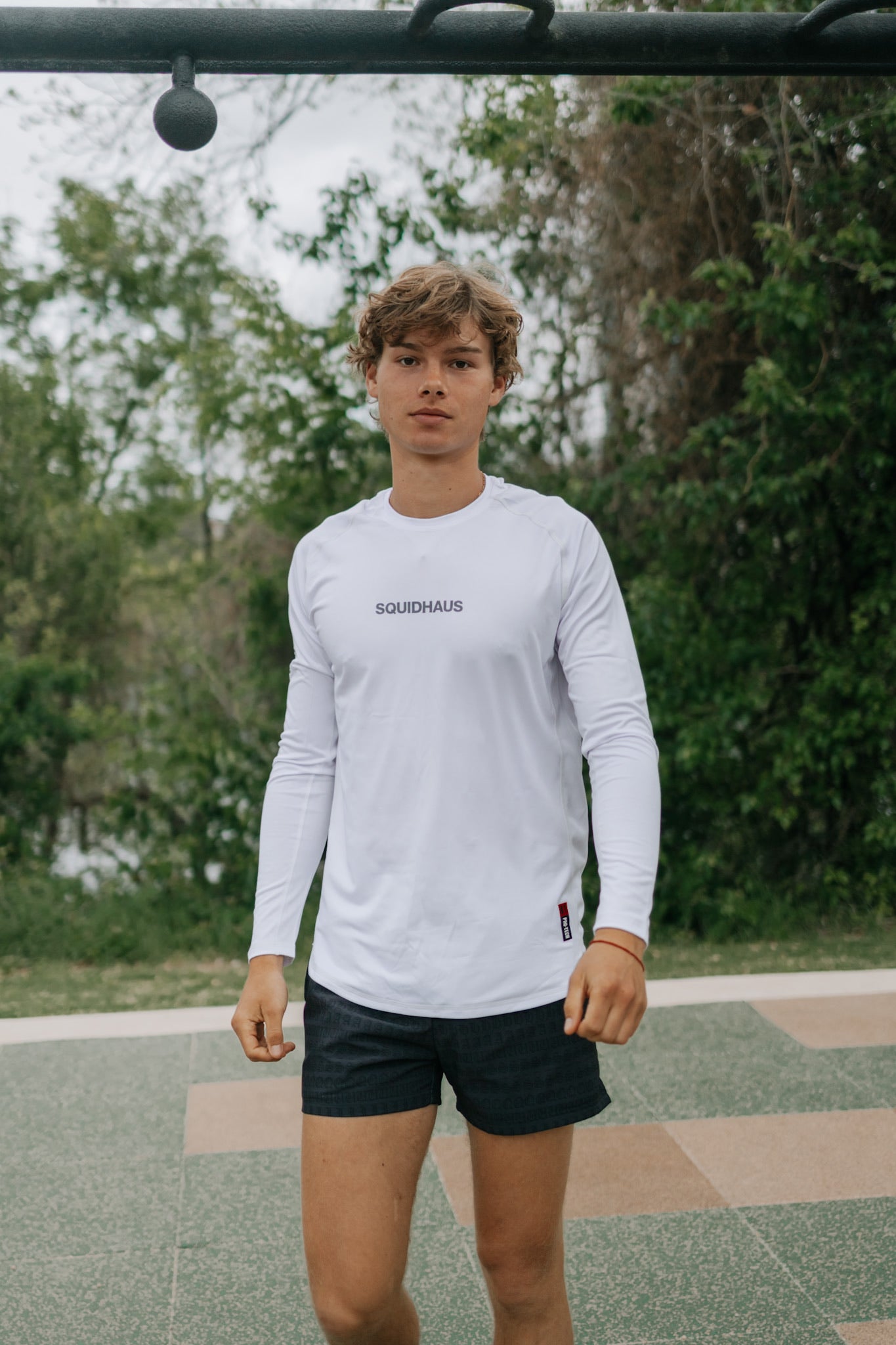 A man wearing a white Pro-Tech V1 Athletic Fitted Long Sleeve Tee by SquidHaus