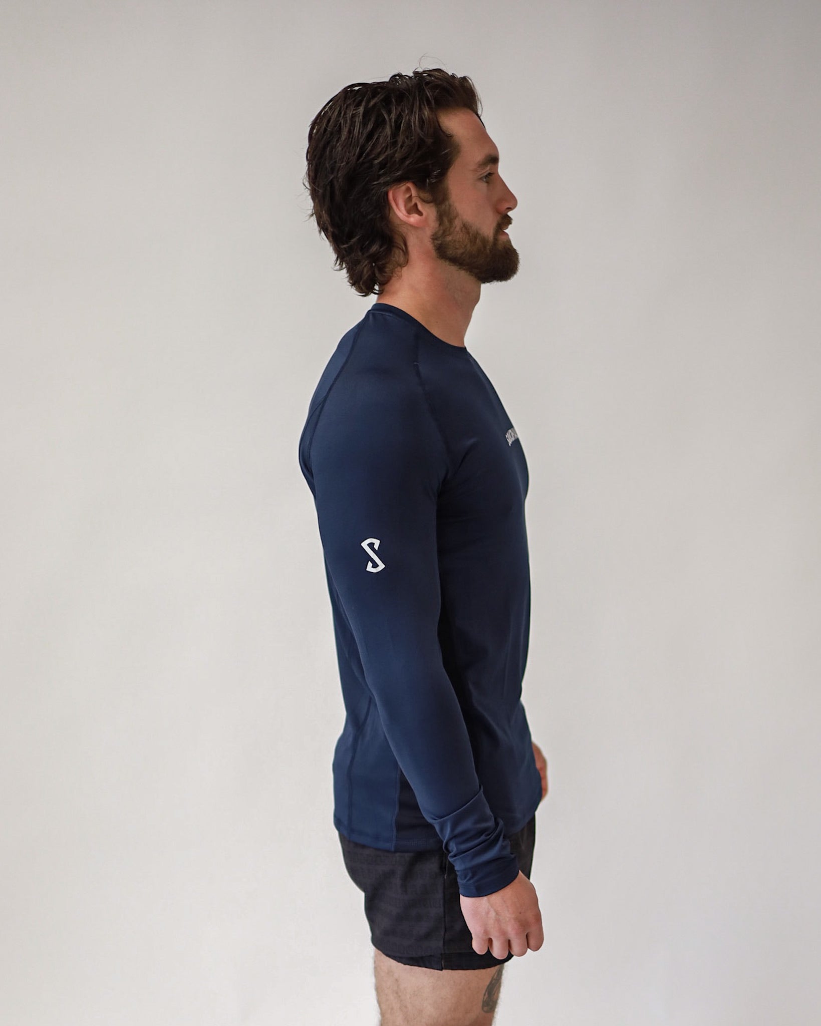 A side view of an athlete wearing a Pro-Tech V1 athletic-fitted long sleeve t-shirt in navy blue and 4" inseam mesh shorts in black, both from SquidHaus