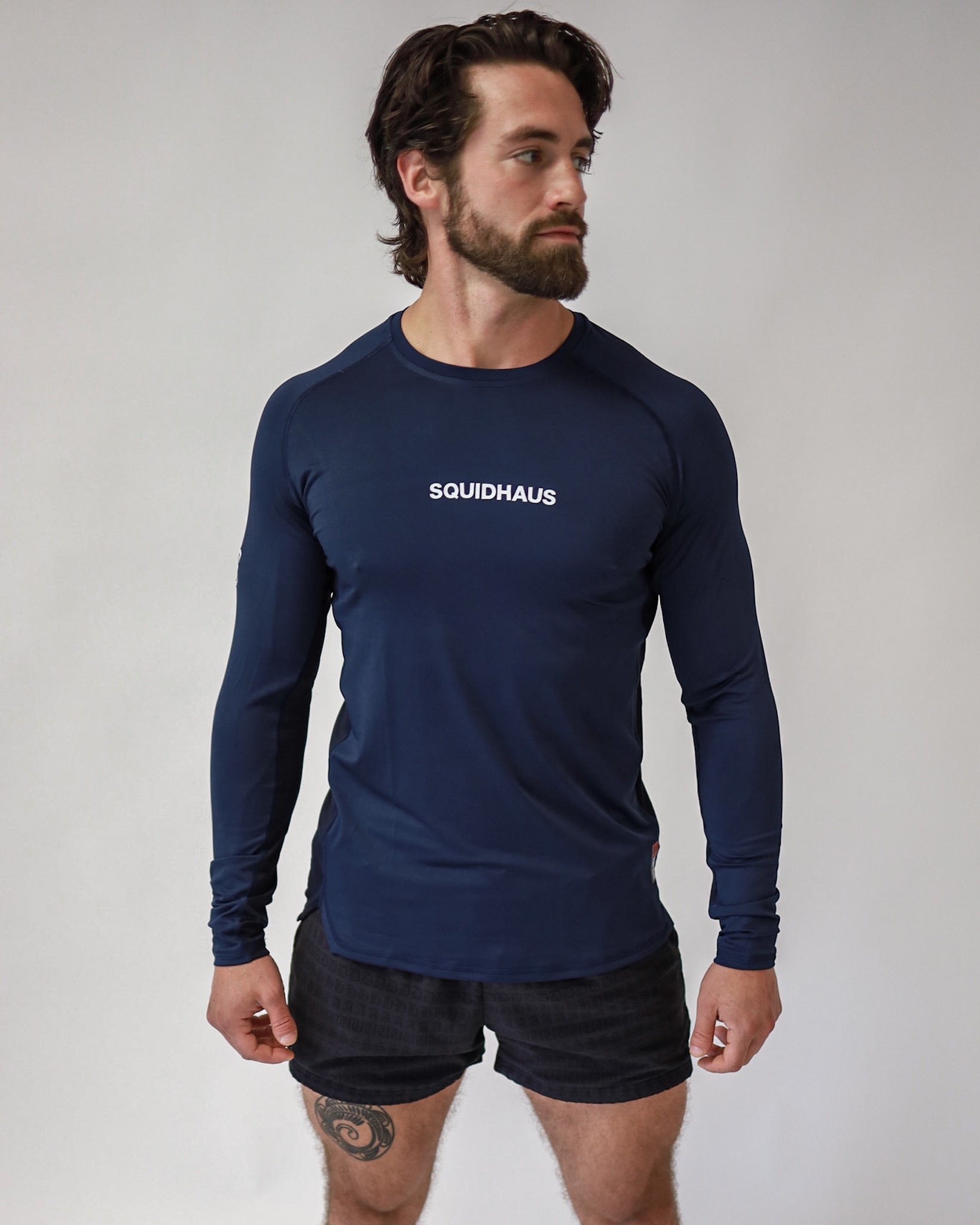 An athletic man wearing a Pro-Tech V1 athletic-fitted long sleeve t-shirt in navy blue and 4" inseam mesh shorts in black, both from SquidHaus